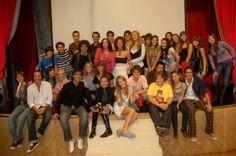 a group of young people posing for a photo on stage with red curtains in the background