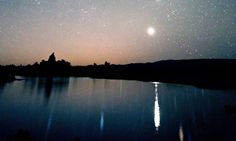 the night sky is filled with stars and reflecting in the water's surface, as seen from across the lake