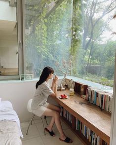 a woman sitting at a desk in front of a window looking out onto the woods