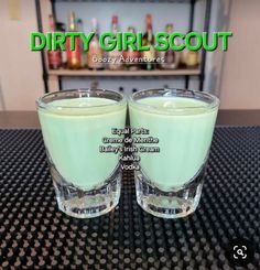 two glasses filled with green liquid sitting on top of a black table next to each other