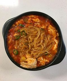 a black bowl filled with noodles and meat on top of a table next to a white counter