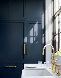 a bathroom sink sitting under a window next to a blue cabinet with gold handles and knobs