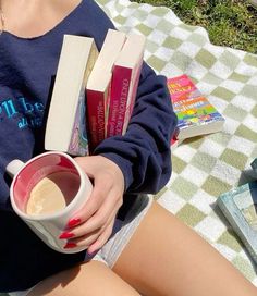 a woman sitting on the grass holding a cup of coffee and books