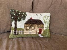 a couch with a pillow on it that has a small house and trees on it