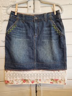 a denim skirt with flowers and lace on the bottom, hanging from a hanger