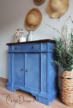 a blue dresser with two hats hanging on the wall and a basket next to it