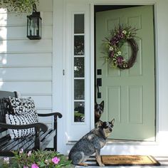 a dog sitting in front of a door with a wreath on it's side