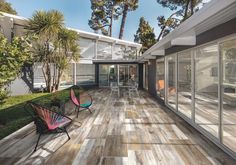 an outdoor deck with chairs and tables next to trees on the side of a house