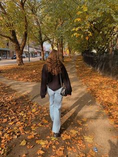 a woman walking down a leaf covered sidewalk