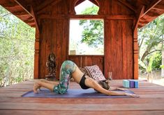 a woman is doing yoga on a blue mat in front of a wooden structure with windows