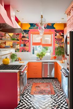 an orange and pink kitchen with black and white tile flooring, stainless steel appliances and colorful wallpaper