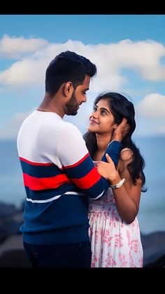 a man and woman standing next to each other near the ocean on a sunny day