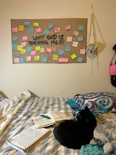 a black cat laying on top of a bed next to a wall with post it notes