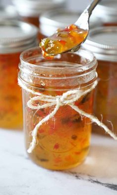 a spoon full of pickled fruit sits on top of a jar filled with jam