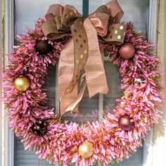 a wreath with pink and gold decorations hanging on the front door to welcome someone in their home