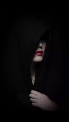 a woman with red lipstick and black hoodie in the dark, holding her hands on her chest