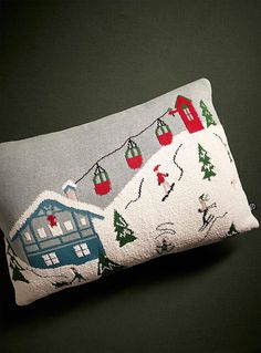 a pillow with christmas decorations on it and a blue house in the snow behind it