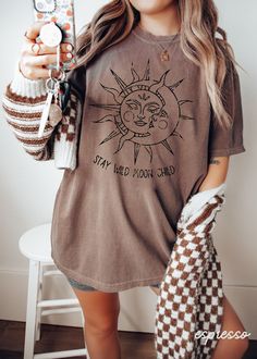 a woman holding up a cell phone and wearing a brown shirt with the sun on it