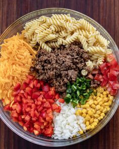 pasta salad with ground beef, tomatoes, onions and cheese in a glass bowl on a wooden table