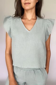 A woman modeling a sea blue cotton gauze ruffled sleeve top with matching pants Cotton V-neck Blouse For Loungewear, Relaxed Fit Ruffle Sleeve Tops For Daywear, Trendy Cotton Tops For Relaxation, Comfortable Summer Tops For Daywear, Cotton Flutter Sleeve Top For Brunch, Summer Tops With Crinkle Texture For Daywear, Summer Crinkle Texture Top For Daywear, Relaxed Fit Tops With Ruffles And Flutter Sleeves, Chic Cotton Tops With Crinkle Texture