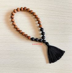 "Sandalwood and Lava Mala Bracelet -  27 + 1 Beads in Knotted Mala with Tassel Sandalwood is a very sacred wood and used widely in Puja/prayer. It has many medicinal properties. It creates a soothing atmosphere around us. It reduces stress and generates positivity. Prayers using Sandalwood beads are said to improve over all well being of a person. Lava is a gemstone that signifies Strength, Courage, Creativity and Calmness. As Lava is formed under extreme conditions of heat and pressure, we can understand that Lava helps us by providing stability in times of change. It provides us with Courage and Strength. It also helps in keeping us Calm, and diminishing our anger. It is a grounding stone, and helps us in connecting with Mother Earth. It is associated with Root Chakra. --> Mala Bracelet Adjustable Wooden Beaded Bracelets With 8mm Beads, Adjustable Wooden Beaded Bracelet With 8mm Beads, Adjustable Wooden Beaded Bracelets For Meditation, Meditation Rosary Bracelet With Wooden Beads, Wooden Beads Rosary Bracelet For Meditation, Brown Wooden Beaded Bracelets With 8mm Beads, Brown Beaded Bracelets With 8mm Beads For Meditation, Brown Rosary Bracelet With 8mm Beads For Meditation, Brown Rosary Bracelet For Meditation