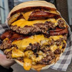 a person holding up a large hamburger with bacon and cheese