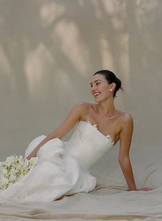 a woman in a white dress is sitting on the floor with her bouquet and smiling