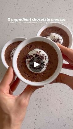 two hands holding small white cups filled with chocolate mousse