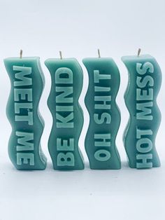 three teal candles with words on them sitting side by side in front of a white background