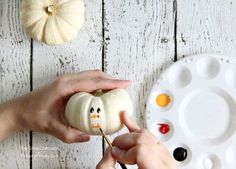 someone is painting a pumpkin with acrylic paint on it and another hand holding one