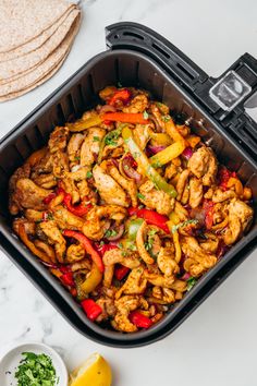 a pan filled with chicken and vegetables next to some pita bread on the side