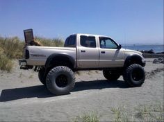 a white truck parked on top of a sandy beach next to the ocean and grass