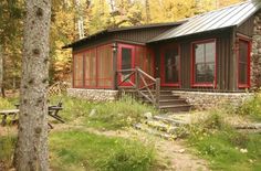 a small cabin in the woods with red windows and stairs leading up to it's front door