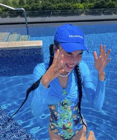 a woman in a blue shirt and hat sitting on the edge of a swimming pool