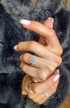 a woman's hand with two rings on it and a fur coat behind her