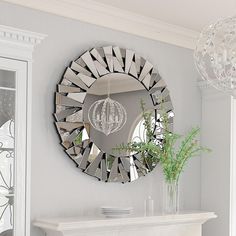 a mirror hanging on the wall above a fireplace with a vase and flowers in it