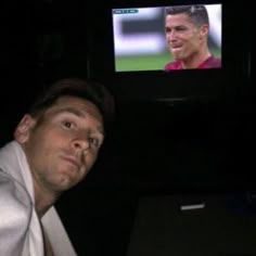 a man in a white shirt is looking at a television screen with a soccer player on it