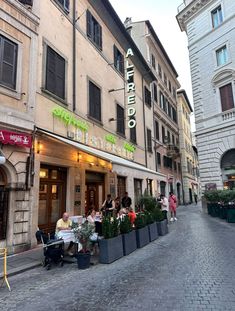 people are sitting at tables in front of a restaurant on a cobblestone street