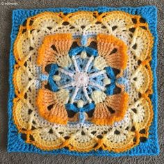 a crocheted square with an orange, blue and yellow flower on it's center