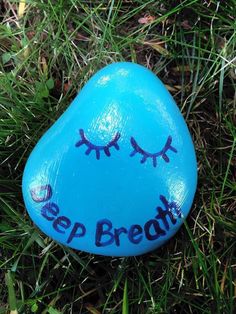 a blue painted rock with eyelashes and the words sleep breath on it sitting in grass