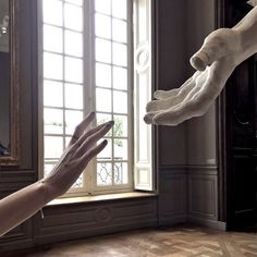 two hands reaching out towards each other in front of a window with a dog statue on it