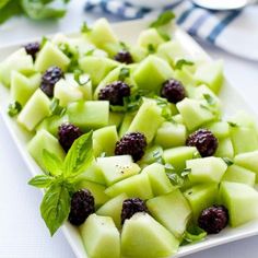 a white plate topped with sliced up fruit and garnished with minty leaves