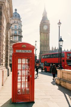 a red phone booth sitting on the side of a road next to a tall clock tower