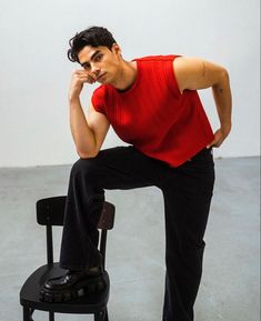 a man sitting on top of a black chair next to a white wall and holding his hand near his face