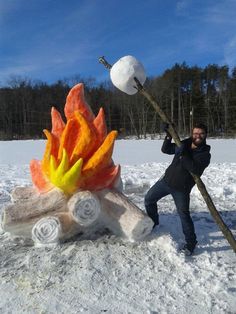 a man holding a stick next to a fake fire and marshmallows in the snow