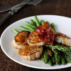 scallops, asparagus and bacon on a white plate next to silverware