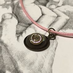 a necklace with a button on it sitting on top of a piece of paper next to a drawing