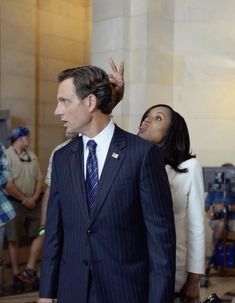 a man in a suit and tie standing next to a woman with her hand up