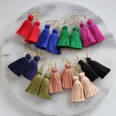 the tasseled earrings are in different colors and sizes on a marble platter