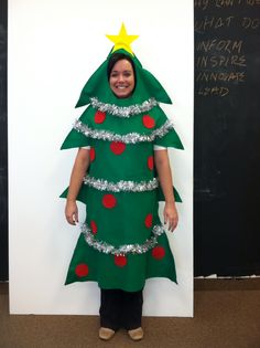 a woman in a christmas tree costume standing next to a chalkboard with writing on it